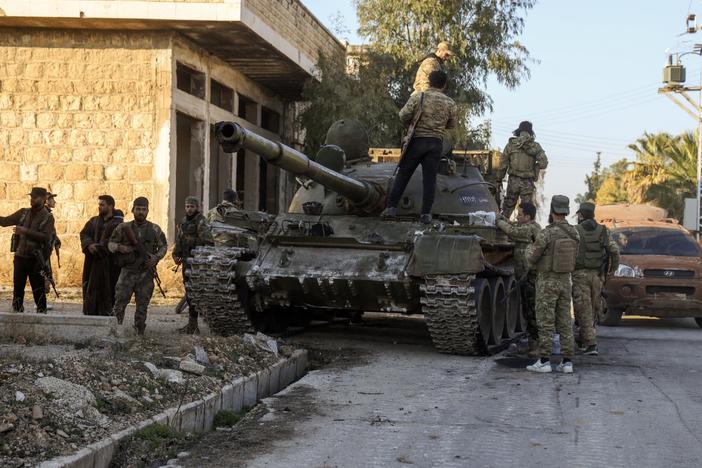 Syrian opposition fighters stand atop a captured Syrian army tank in the town of Maarat al-Numan, southwest from Aleppo, Syria, Saturday.