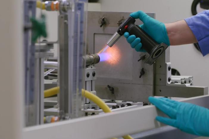 Engineer Matt Gwin puts a piece of aerogel material inside a metal frame and ignites it. After a minute or two, the material is intact and only feels warm.