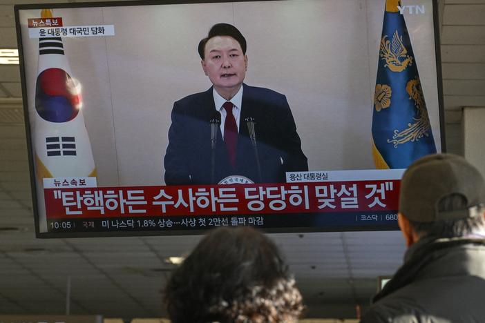 People watch a screen showing South Korean President Yoon Suk Yeol speaking during a televised address at a bus terminal in Seoul on Dec. 12, 2024.