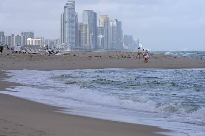 People walk along the beach in Surfside, Fla., near the skyline of Sunny Isles Beach, on Dec. 17, 2024.