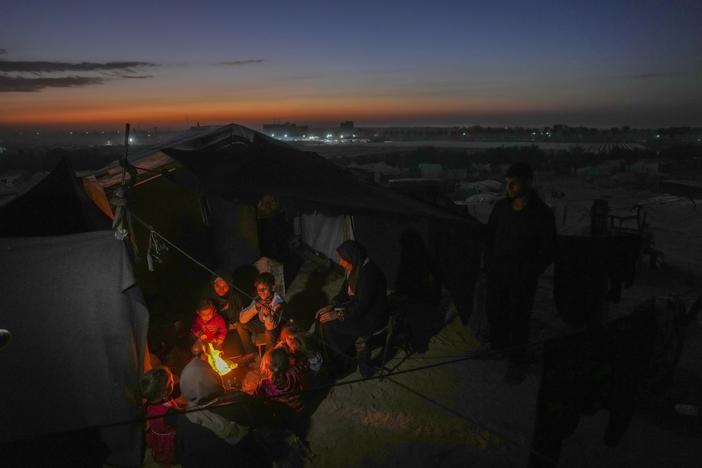 Reda Abu Zarada, 50, displaced from Jabaliya in nothern Gaza, sits by a fire with her grandchildren at a camp by the sea in Khan Younis, Gaza Strip, Thursday, Dec. 19, 2024.