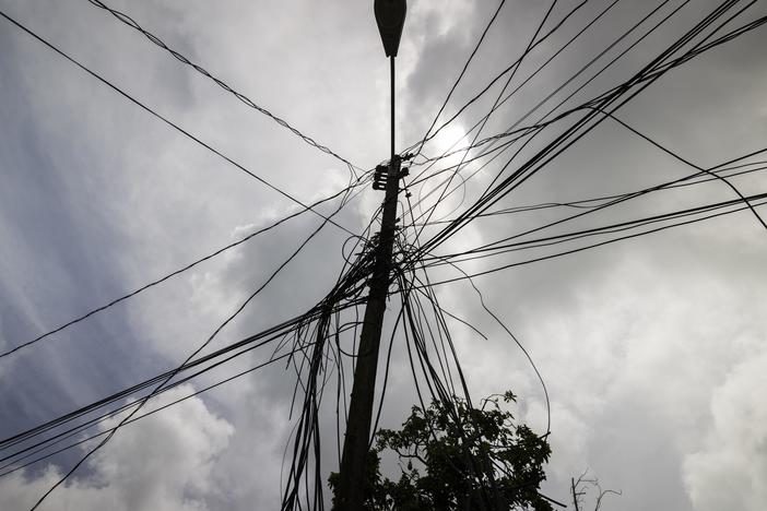 A utility pole with loose cables is shown towering over a home in Loiza, Puerto Rico, Sept. 15, 2022.