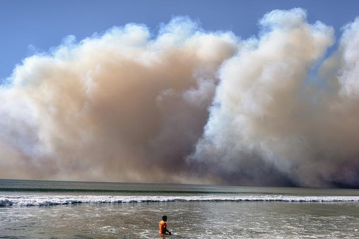 A swimmer watches as a large dark plume of smoke passes over the beach from a wildfire from Pacific Palisades, in Santa Monica, Calif., Tuesday, Jan. 7, 2025. (AP Photo/Richard Vogel)
