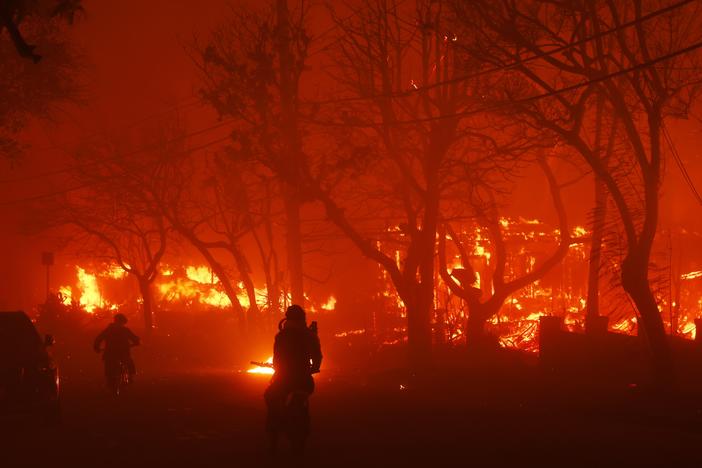 Two persons ride by on motorcycles as the Palisades Fire destroys a neighborhood in the Pacific Palisades neighborhood of Los Angeles on Tuesday, Jan. 7, 2025.