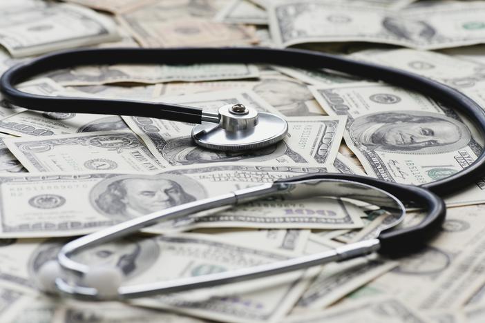 A stethoscope sits on a pile of U.S. bank notes.
