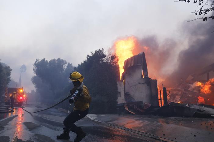 A firefighter battles the advancing Palisades Fire as it burns a structure in the Pacific Palisades neighborhood of Los Angeles on Tuesday.