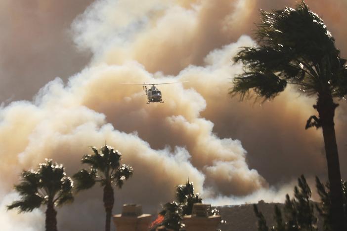 Palm trees are bent from the wind as a helicopter flies above homes threatened by the wind-driven Palisades fire in Pacific Palisades, Calif., on Tuesday.