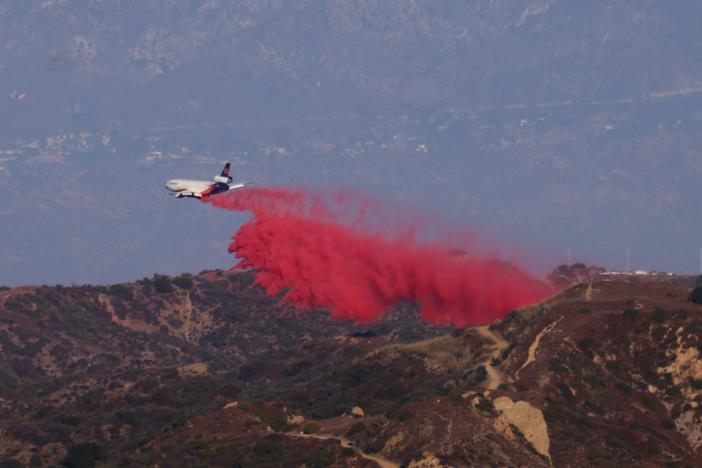 A tanker drops retardant as the Palisades Fire grows in the mountains in Topanga, Calif., on Thursday