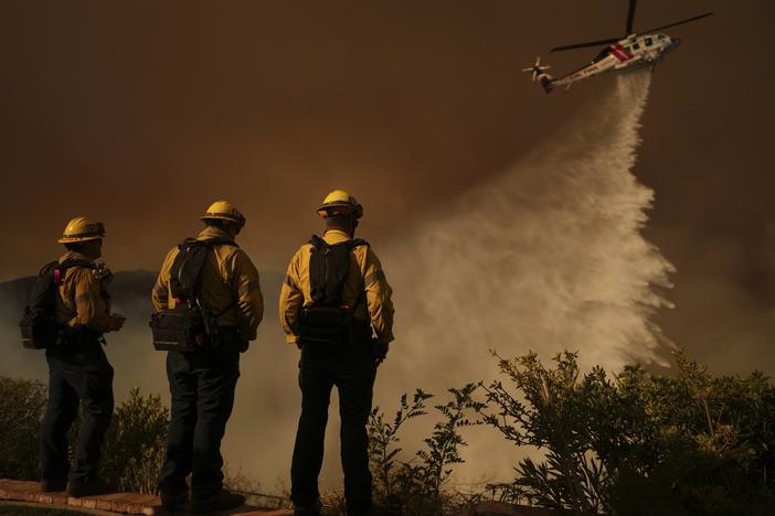 A helicopter drops water on Mandeville Canyon as the Palisades Fire rages Saturday in Los Angeles.