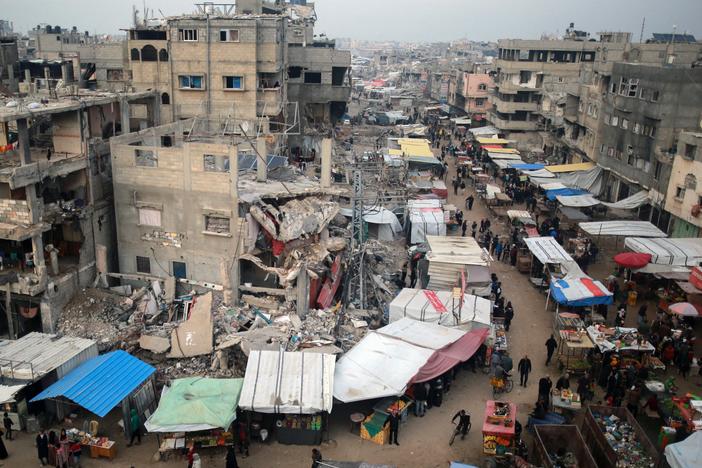 People walk past stalls selling goods amid the rubble of buildings destroyed during previous Israeli strikes, in Khan Yunis in the southern Gaza Strip on January 15, 2025.