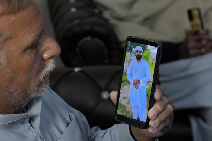 A Pakistani Mohammad Akram shows a picture of his son Abu Bakar,  one of the victims of a migrant boat that capsized in West Africa's Atlantic coastline,  on his cell phone at his home, in Jura village, in the Lalamusa district in Pakistan, on Friday.