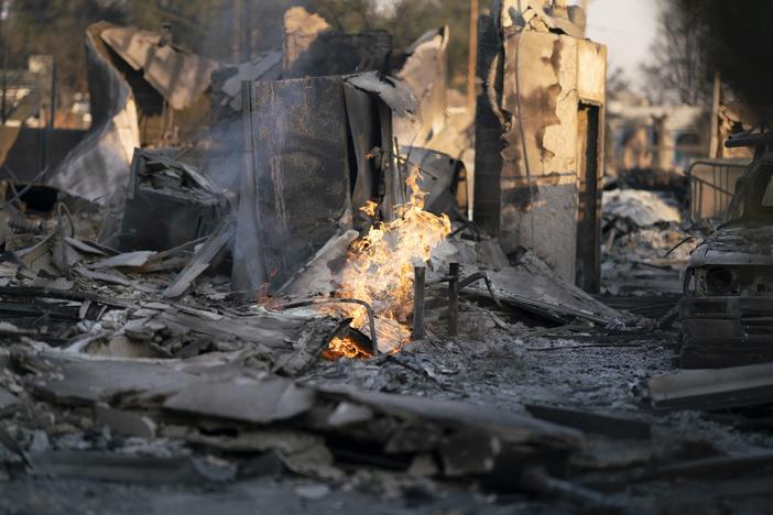 Some gas lines were still burning in Altadena, California, after the Eaton fire passed through a burned neighborhood. Crews were working to cut off gas to the area. Smoke and ash from the LA-area fires blanketed the region. Experts suggest care while cleaning up, even far from the immediate burn zones.