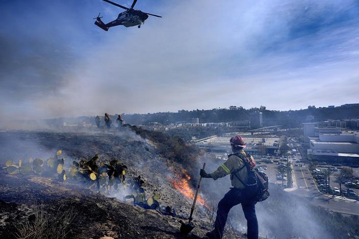 San Diego firefighters knock down a small brush along a hillside over the Mission Valley Shopping Mall in San Diego on Tuesday.
