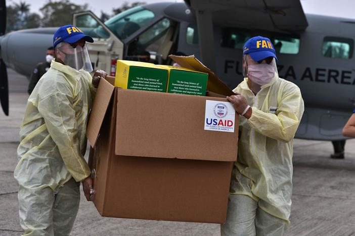 After being inaugurated for his second president term, President Donald Trump has frozen virtually all U.S. foreign aid and issued a "stop work" order for groups in other countries that are funded by the U.S. government. Above: At the start of the pandemic, members of the Honduran Armed Forces carry a box containing diagnostic kits to test for COVID-19, donated by the United States Agency for International Development and the International Organization for Migration.