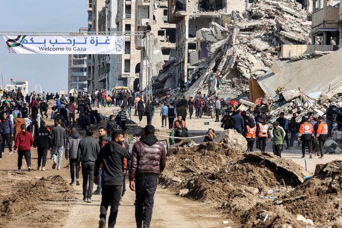 People gather by a banner welcoming people near the rubble of a collapsed building along Gaza's coastal al-Rashid Street for people to cross from the Israeli-blocked Netzarim corridor from the southern Gaza Strip into Gaza City on Sunday.