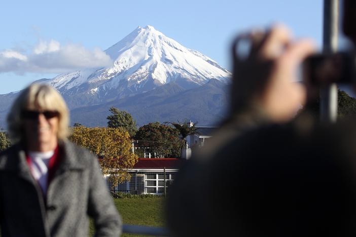 A man takes a picture of his wife with Mount Taranaki, also known as Mount Egmont, in the background in New Plymouth, New Zealand.