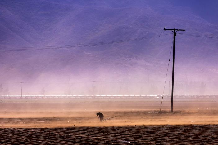 A farmworker laboring through high winds near a brush fire in Camarillo, CA on Jan.23, 2005. Employers in California are legally required to provide N95 respirators to workers when the Air Quality Index reaches 150.