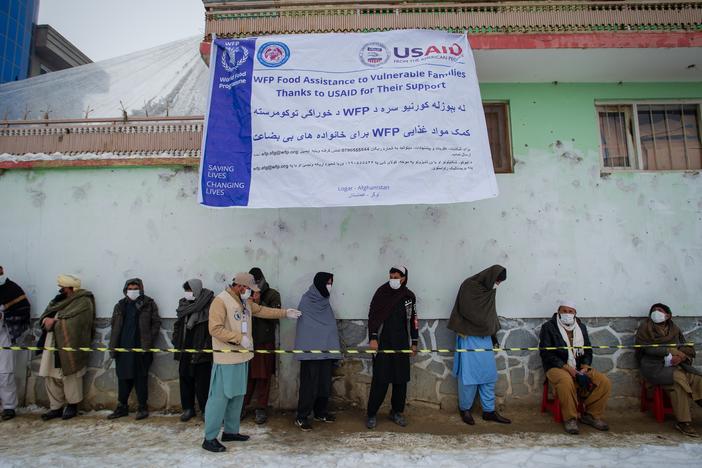 Afghan men wearing masks to prevent the spread of COVID-19 line up as the U.N.'s World Food Program (WFP) distributes a monthly food ration to address fears of looming famine due to drought and winter conditions. Food for this delivery in January 2022 was largely supplied by the U.S. Agency for International Development (USAID).