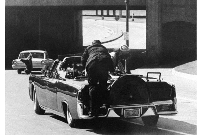President John F. Kennedy slumps down in the back seat of the presidential limousine as it speeds along Elm Street toward the Stemmons Freeway overpass in Dallas, Texas, after being fatally shot, Nov. 22, 1963. First lady Jacqueline Kennedy leans over the president as Secret Service Agent Clint Hill pushes her back to her seat.