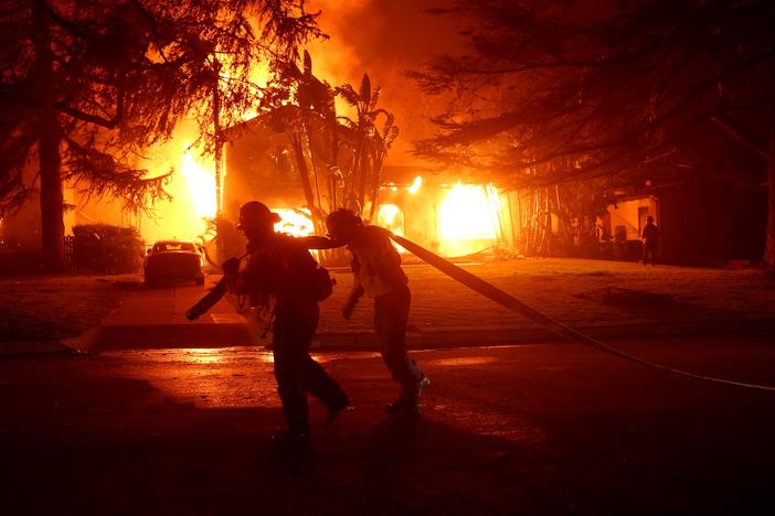 Los Angeles County firefighters pull a hose in front of a burning home as the Eaton Fire moved through the area on Jan. 8 in Altadena, Calif.