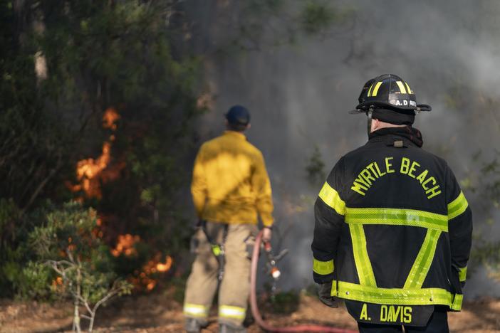 Firefighters attend to a flare-up in the Carolina Forest neighborhood on Sunday in Myrtle Beach, S.C. Multiple forest fires in the area caused evacuations along the South Carolina coast. A storm is expected to bring extreme weather and wildfire risk to various regions across the U.S. this week.