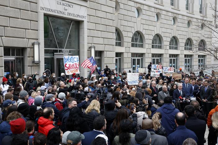 The Trump administration's plans for mass firings are sparking protests and challenges in court. Here, supporters of the U.S. Agency for International Development join Sen. Chris Van Hollen, D-Md., and Rep. Gerry Connolly, D-Va., outside USAID's headquarters in Washington, D.C., on Feb. 3 after Elon Musk, who oversees the Department of Government Efficiency, said he and President Trump would close the foreign assistance agency.