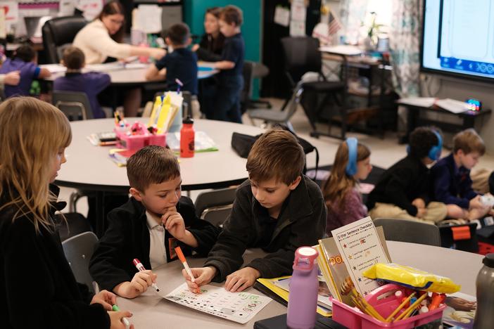 Second graders Serena Lacour, Luke Busby and Dylan Poche work on a word-identification reading game, while other groups work with their teacher, Cady Caskey, on sounding out words.