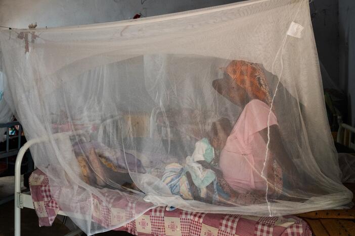 A pregnant woman brought her child to a health clinic in Farchana, Chad. They are sitting under a mosquito net.