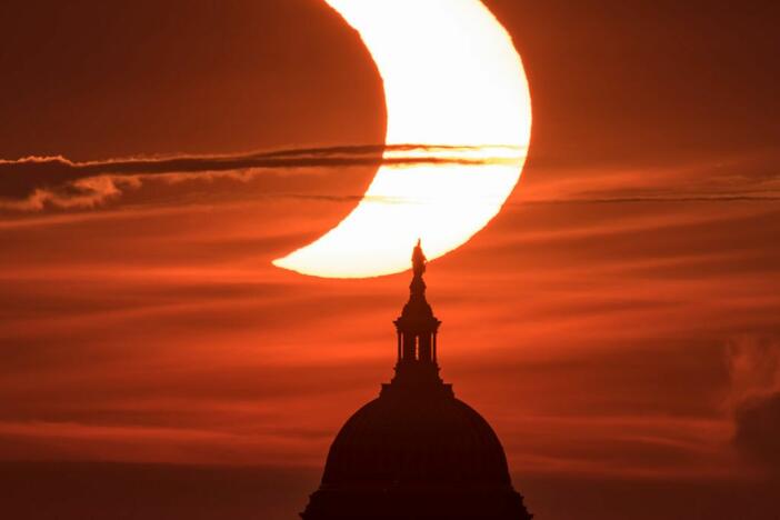A partial solar eclipse is seen as the sun rises behind the U.S. Capitol building on June 10, 2021.