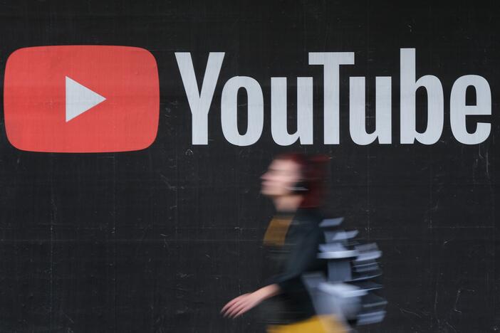 A young woman wearing headphones walks past a billboard advertisement for YouTube in 2019 in Berlin, Germany.