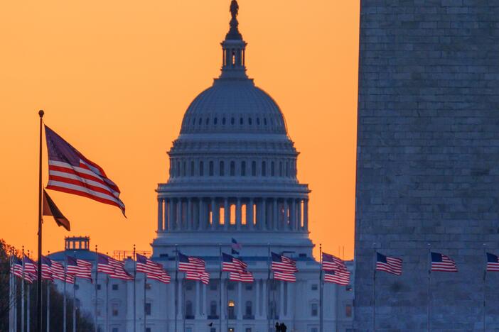 Sunrise turns the sky orange behind the U.S. Capitol building as it illuminates the U.S. flags circling the base of the Washington Monument on March 23 in Washington, D.C.