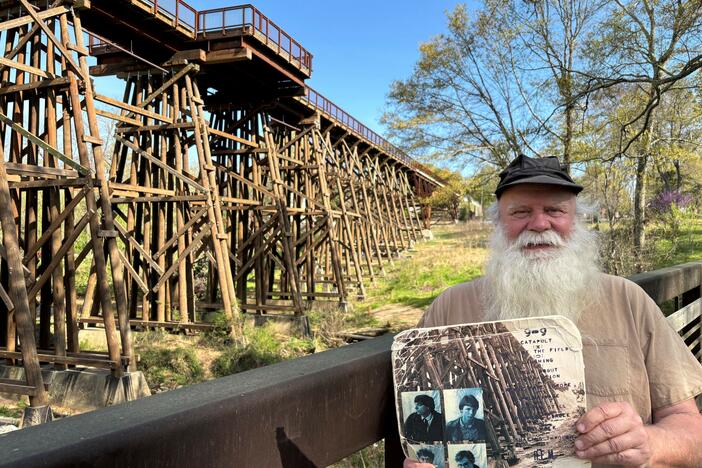 Paul Butchart gives tours of musical landmarks all over Athens, Ga. In his hands is R.E.M.'s 1983 <em>Murmur</em> album, with the original trestle bridge photograph on the back cover. The bridge behind Butchart is a reconstruction, and now part of a walking and biking trail.