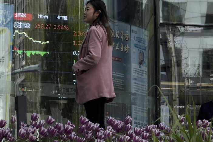 People stand outside a brokerage house, as an electronic board displays shares trading, in the Central Business District in Beijing on Thursday.
