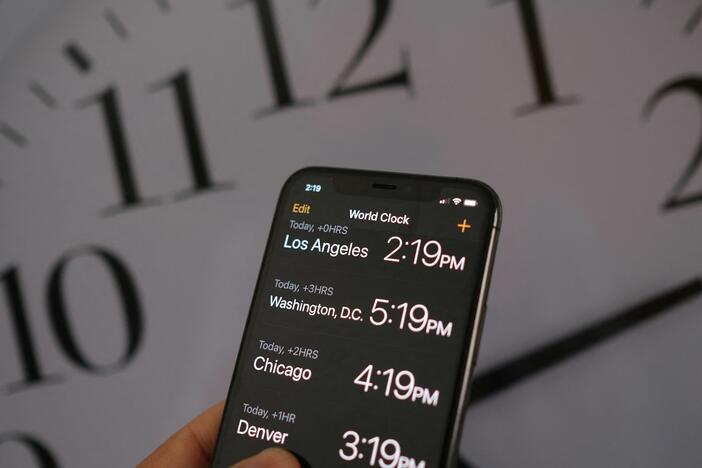 This illustration photo shows a clock in the background of a smartphone showing the time after daylight saving time was implemented in Los Angeles, Calif., on March 15, 2022.