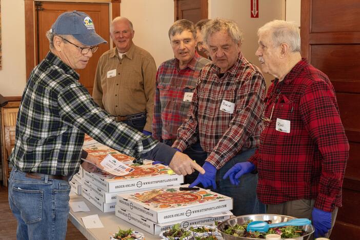 Attendance has more than quadrupled since the free ROMEO lunches for older men started in Harpswell, Maine, last fall. Tom Mahoney, left, directs other volunteers at a recent lunch when pizza was on the menu.