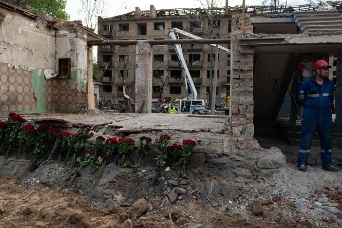 Rescue workers stand near a destroyed building, where roses are placed in Kyiv, Ukraine, in tribute to the victims of the Russian rocket attack the day before, on April 24.