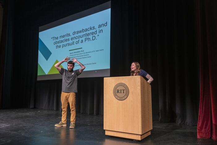 Growing up, Sara Blick-Nitko says she "didn't see role models" who were deaf working in science. Now she tells students—here, on stage with an American Sign Language interpreter—how a series of federal grants, known as the "Deaf Scientist Pipeline," helped her get her Ph.D. and work in a lab researching  treatments for cancer.