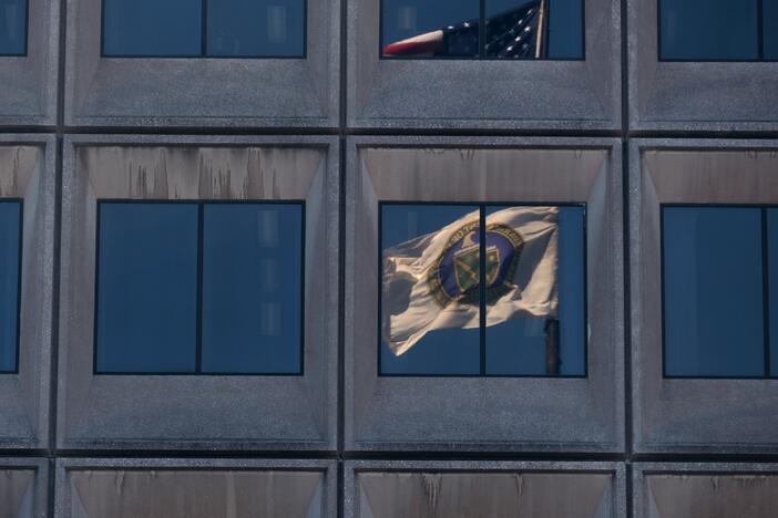 The reflection of the flag of the U.S. Department of Energy is seen on the department's headquarters building in Washington, D.C., in March. The Joint Office of Energy and Transportation, a unique government body designed to bring together expertise from the Department of Energy and the Department of Transportation, has been affected deeply by government-wide efforts to cut jobs. Former staffers say there are no full-time federal employees remaining at the Joint Office.
