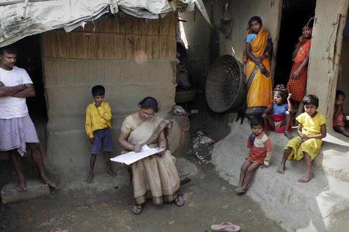 Mahesh Shah, left, stands as his family members look while census worker Rumima Das, writes the information on a paper on the first day of the national census at Ramsingh Chapori village, east of Gauhati, India in 2010.