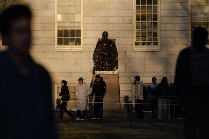 People gather to take photos with the John Harvard statue at Harvard University. President Trump made another threat to Harvard's tax-exempt status in a social media post on Friday.