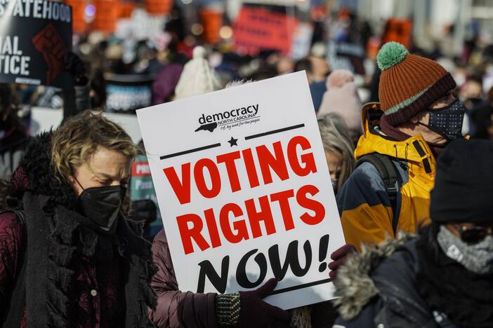 A demonstrator carrying a sign that says "VOTING RIGHTS NOW" walks across the Frederick Douglass Memorial Bridge in 2022 in Washington, D.C.
