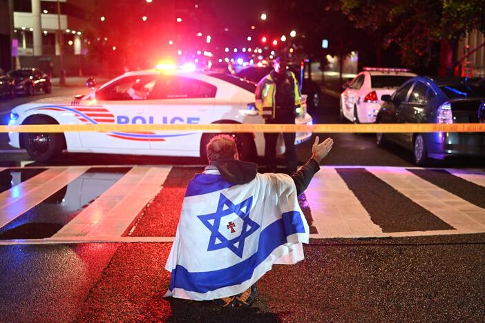 A man draped in the Israeli flag, bearing a cross and the name "Jesus" at its center, gestures as Metropolitan Police officers secure the area outside the Capital Jewish Museum following a shooting that left two people dead in Washington, DC, in the early hours of May 22, 2025.