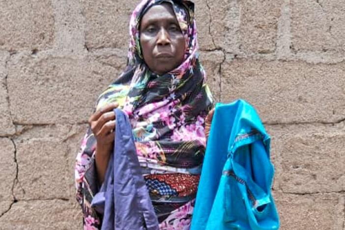 Mariam Mohammed, a widow, stands outside her home in Bama, Nigeria. She's holding her younger son Babagana's favorite clothes. He died in early February from complications of sickle cell disease. She had taken him to a U.S.-funded clinic for treatment, but at that time the facility was shuttered due to a stop-work order issued by the Trump administration.