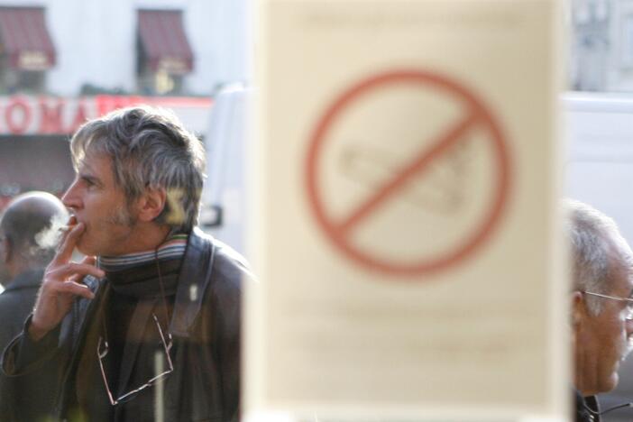 A man smokes a cigarette outside a brasserie, in front of a sticker on a window reading: "Smoking is forbidden."