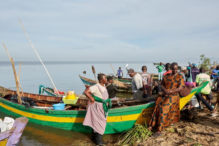 Alice Akinyi (left, hand on hip) and Justine Adhiambo Obura, members of the No Sex For Fish group, stand next to Alice's fishing boat at Nduru Beach. It's one of the few boats that have weathered the storms and floods that have beset the area since 2020.