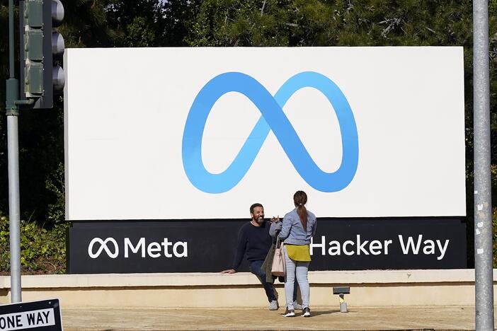 People talk near a Meta sign outside of the company's headquarters in Menlo Park, Calif.