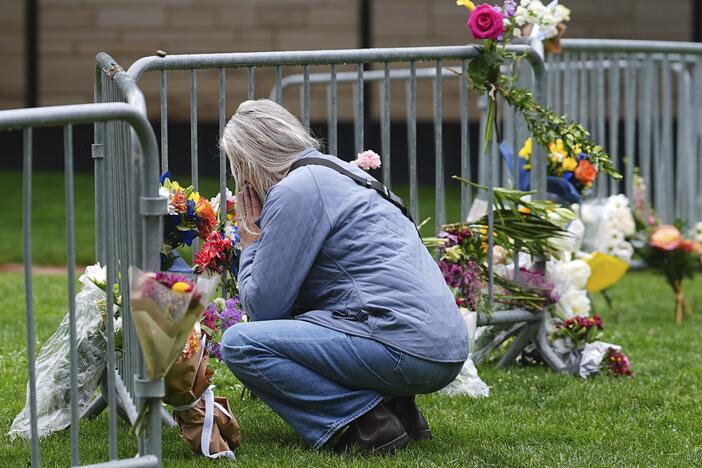 A visitor offers a tribute after leaving a bouquet of flowers at a makeshift memorial for victims of an attack outside of the Boulder County, Colo., courthouse as a light rain falls Tuesday, June 3, 2025, in Boulder, Colo. (AP Photo/David Zalubowski)