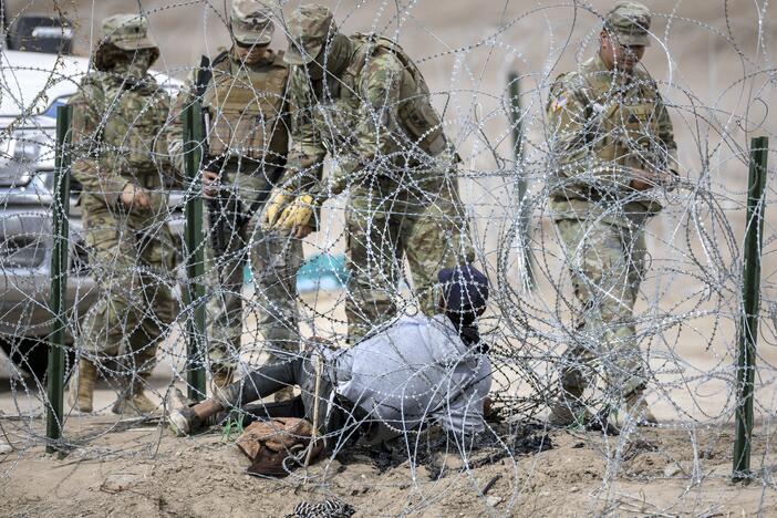 Texas National Guard troops try to untangle an immigrant caught in razor wire after he crossed the U.S.-Mexico border into El Paso, Texas, on Jan. 31, 2024. The Trump administration now plans to use Guard troops for law enforcement activities, including "night operations and rural interdiction," as well as "guard duty and riot control" inside immigrant detention facilities.