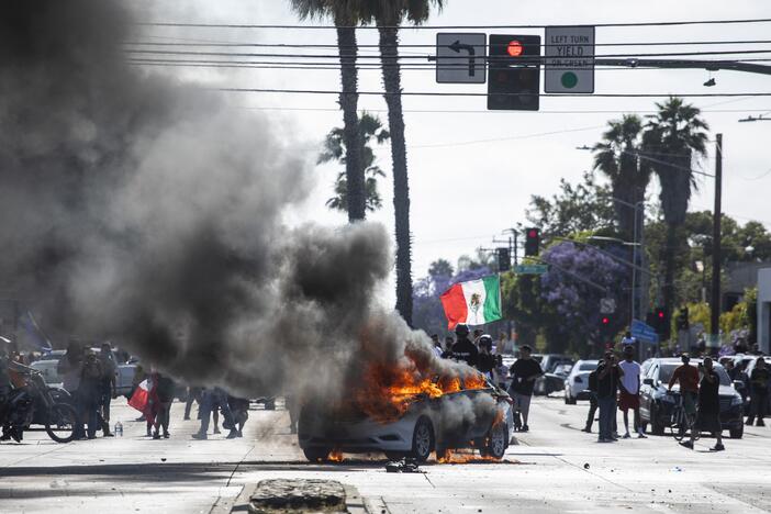 A car burns as a demonstrator waves a Mexican national flag during a protest following federal immigration operations, in the Compton neighborhood of Los Angeles, California, on June 7, 2025.