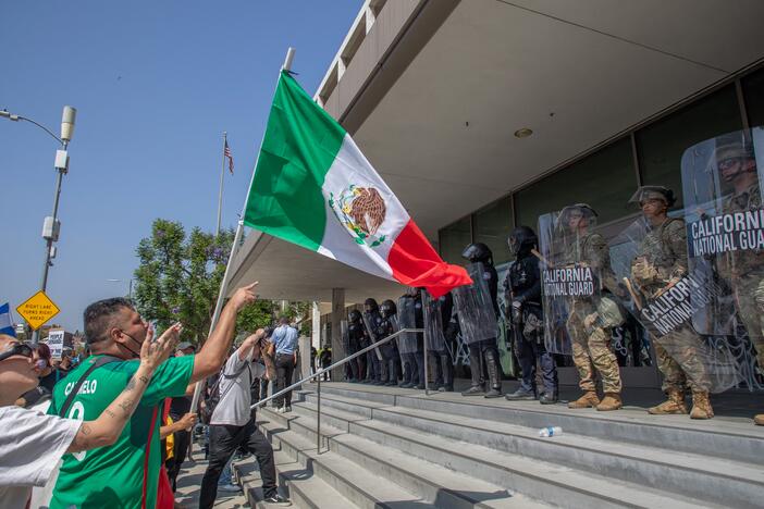 A person waves a Mexican flag in front of California National Guard members standing guard outside a federal building in Los Angeles on Monday.